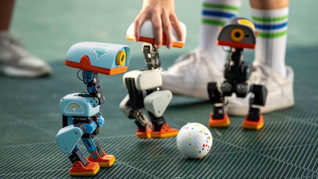 Microduck robot playing with a ball beside two others on a school playground