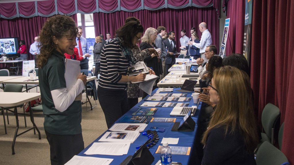 handshake ai skills studio: recruiters and job seekers at a career fair table covered in printed resumes