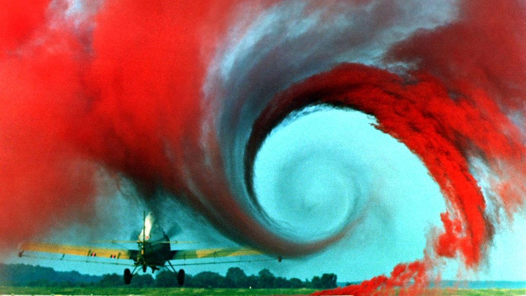 OpenAI Navier Stokes: red smoke reveals a wingtip vortex spiralling inward behind a low-flying aircraft