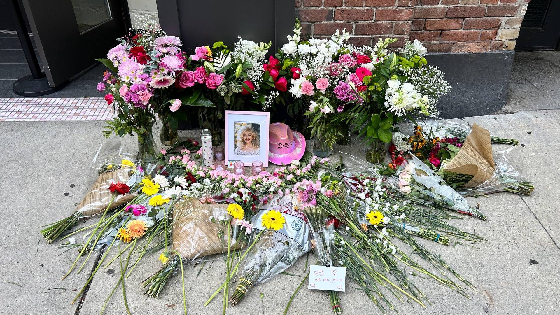 stella parton fake ai content: flowers, candles and a framed photo of Dolly Parton at a memorial outside Dolly's bar in Toronto