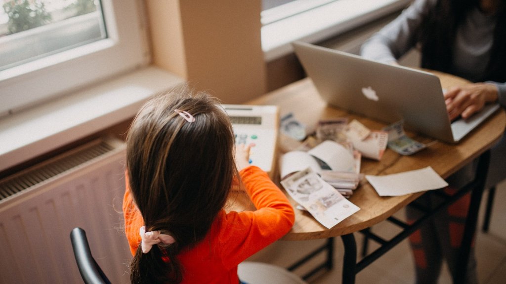 Mumsnet message board AI instructions: a parent types on a laptop at home while a child sits beside her
